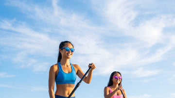 Two women paddleboarding on bright water while wearing performance sunglasses for water-sports glare and stable fit