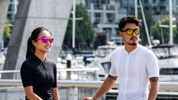 Asian cycling couple wearing 2nu sunglasses in a bright urban marina setting, showing outdoor fit and lens clarity for an online buying review guide